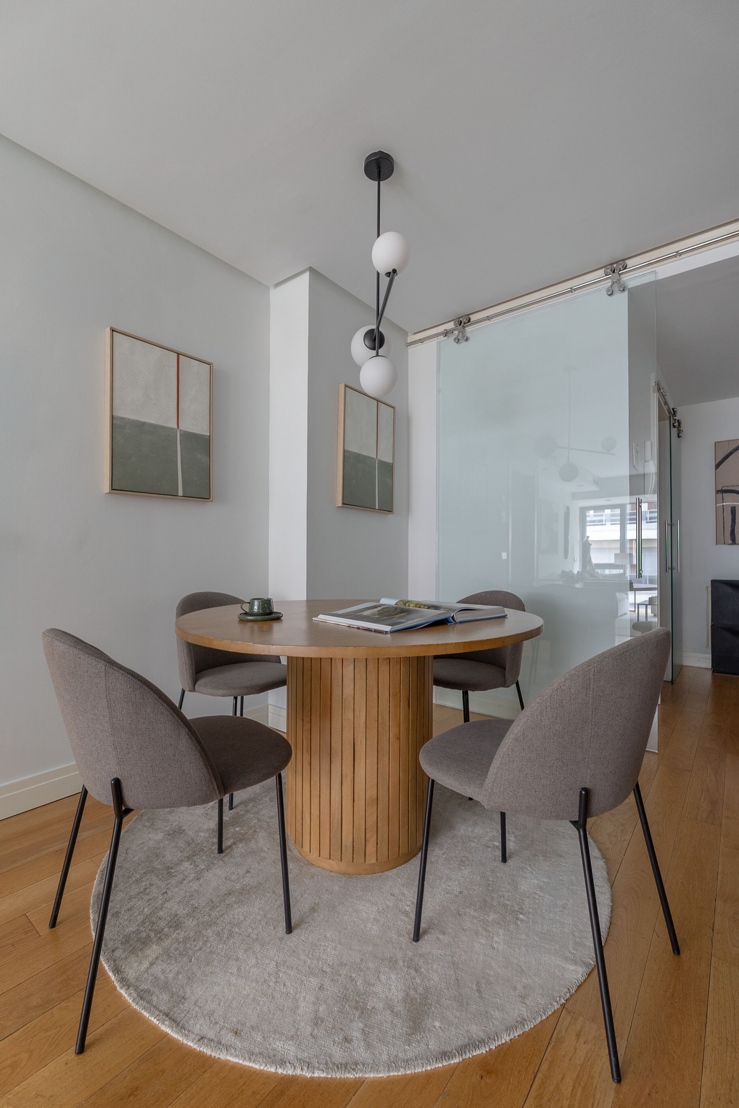 Een moderne eetruimte met een ronde houten tafel, vier grijze stoelen en een centraal hanglamp.