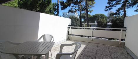 A patio with a table and two chairs, a white railing, and trees in the background.