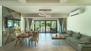 Un salon moderne comprenant un coin repas, un canapé et un téléviseur fixé au mur, qui est recouvert de marbre.