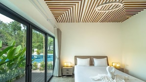 Une chambre d’hôtel moderne dotée d’un grand lit, de deux tables de chevet avec des lampes, d’un plafond orné d’un motif géométrique et d’une porte-fenêtre coulissante donnant sur un espace piscine.
