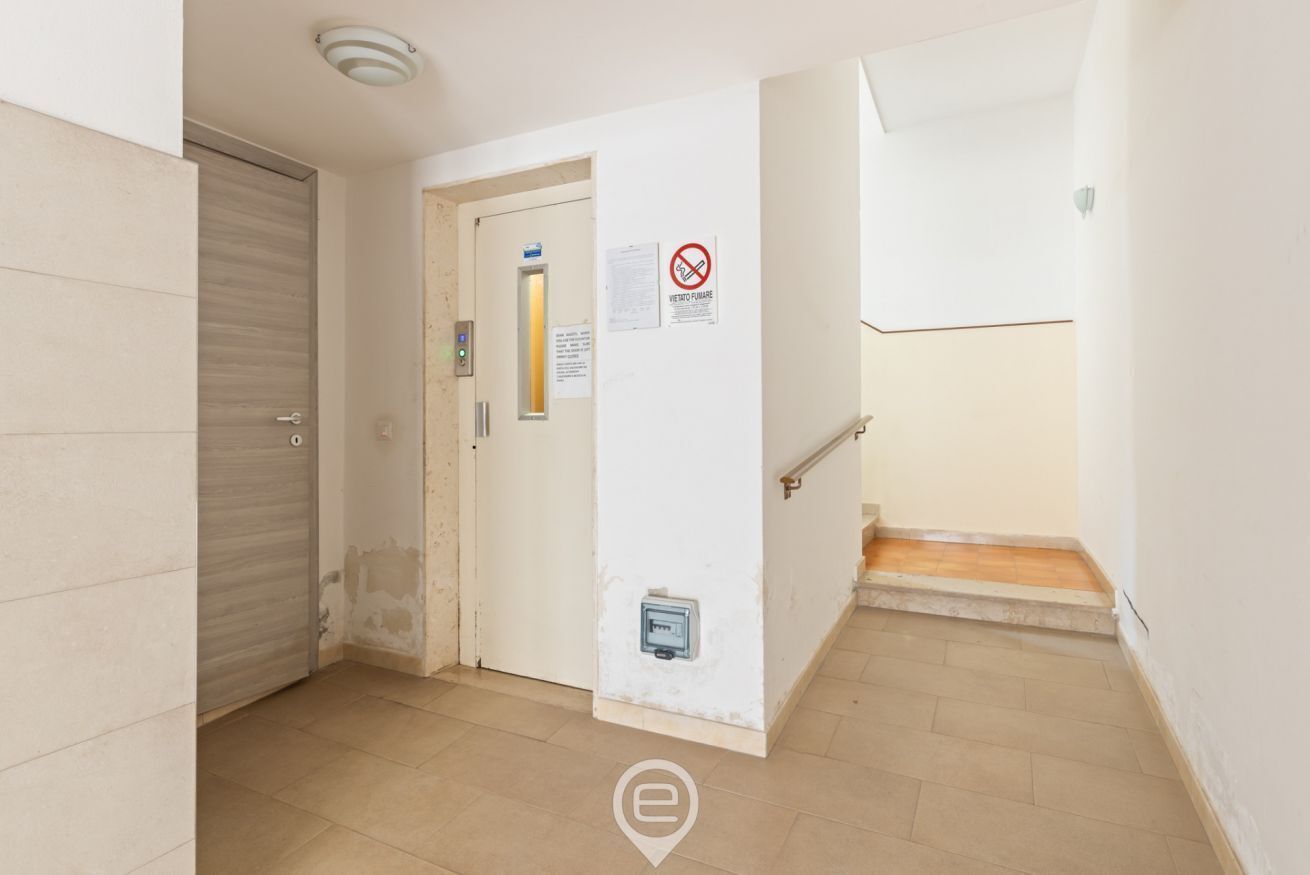 A hallway with a closed door, a staircase, and a wall-mounted electrical outlet.