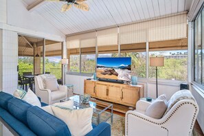 A living room with a television, sofa, and chairs, large windows with blinds, and a view of the outdoors. - Haleakala Shores A-411 - Modern 2BR/2BA, 2 King Beds, Sleeps 4, Split AC, Wi-Fi (Kihei)