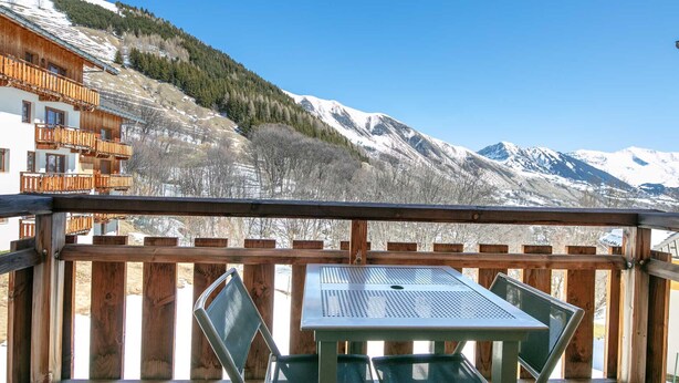 A wooden deck with a table and chairs, overlooking snow-capped mountains and a forested hillside. - Large Family Apartment - Mountain View - Sleeps 7/8 (Saint-Sorlin-d´Arves)