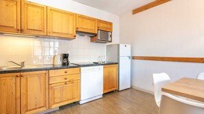 Una cocina con armarios de madera, microondas, refrigerador, lavavajillas y una mesa de comedor con sillas.