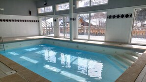 An indoor swimming pool with clear water, a tiled floor, and a view of a snowy landscape through large windows. - Large Family Apartment - Mountain View - Sleeps 7/8 (Saint-Sorlin-d´Arves)