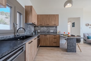 A modern kitchen with wooden cabinets, a granite countertop, and a built-in dishwasher. - Kedros villa Exi , next to the beach and near taverns (Ano Viannos)