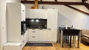 Una cocina compacta con muebles blancos, encimera negra y un rincón comedor con mesa y sillas.