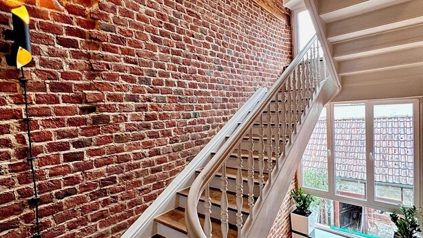 A staircase with white balusters, a brick wall, and a view through a window. - Rebenblick Ferienwohnung (Landau in der Pfalz)