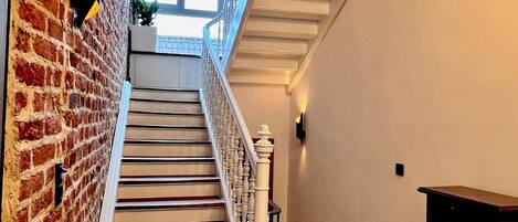 Un escalier avec un sol à carreaux, un mur de briques et une rampe blanche.