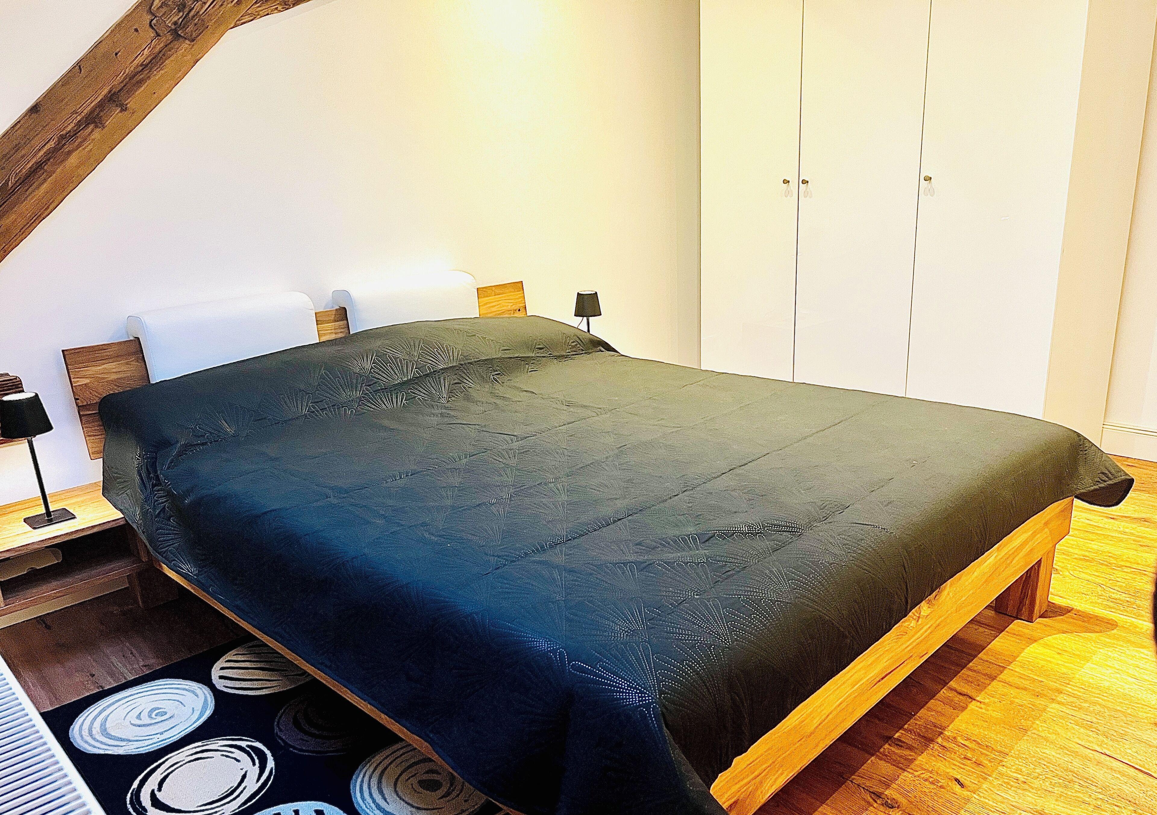 A bedroom with a bed, wooden headboard, bedside tables, a lamp, and a wardrobe.