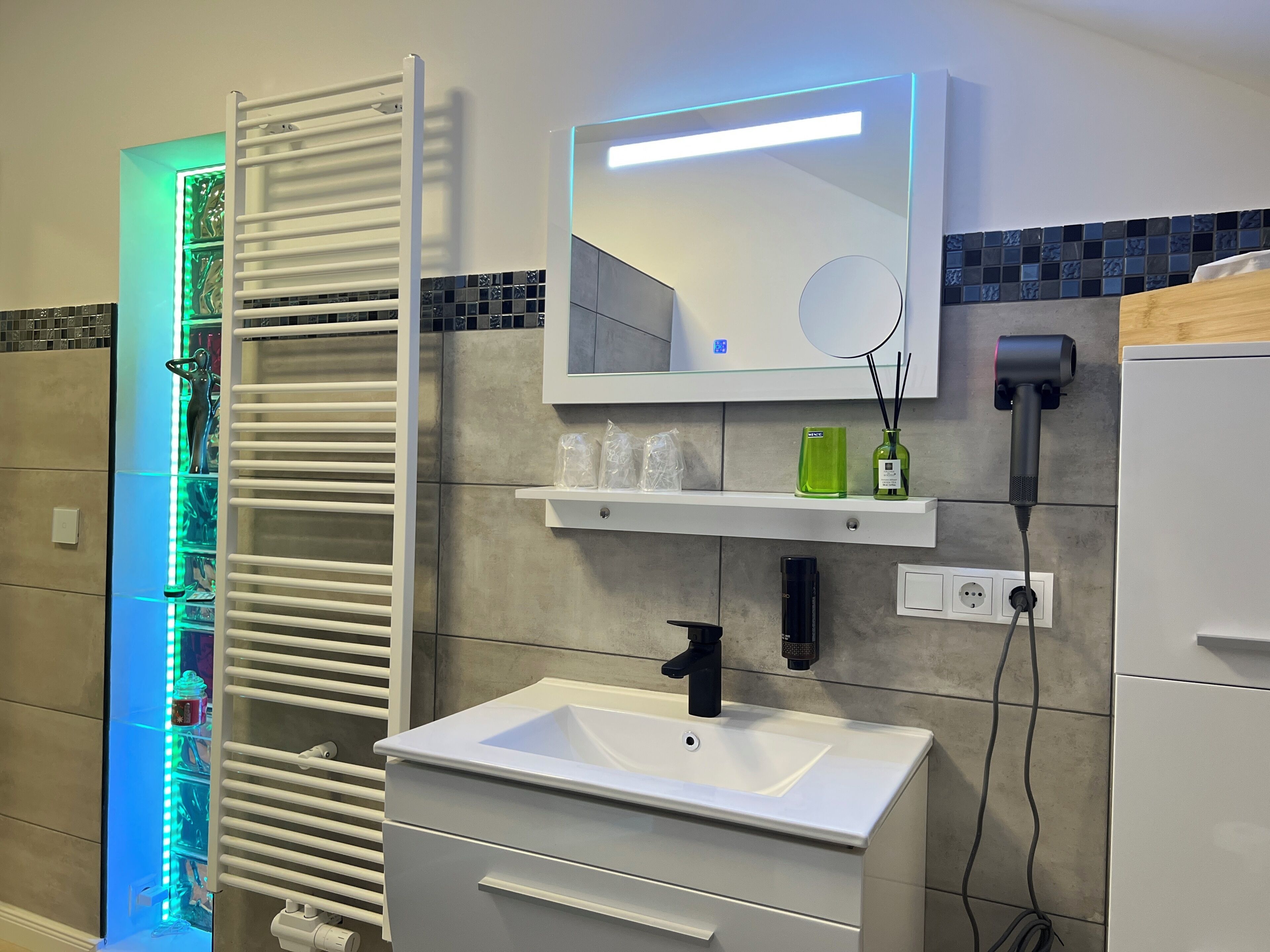 Een badkamer met een wit wastafelmeubel, een spiegel, een handdoekrek en een plank met toiletartikelen.
