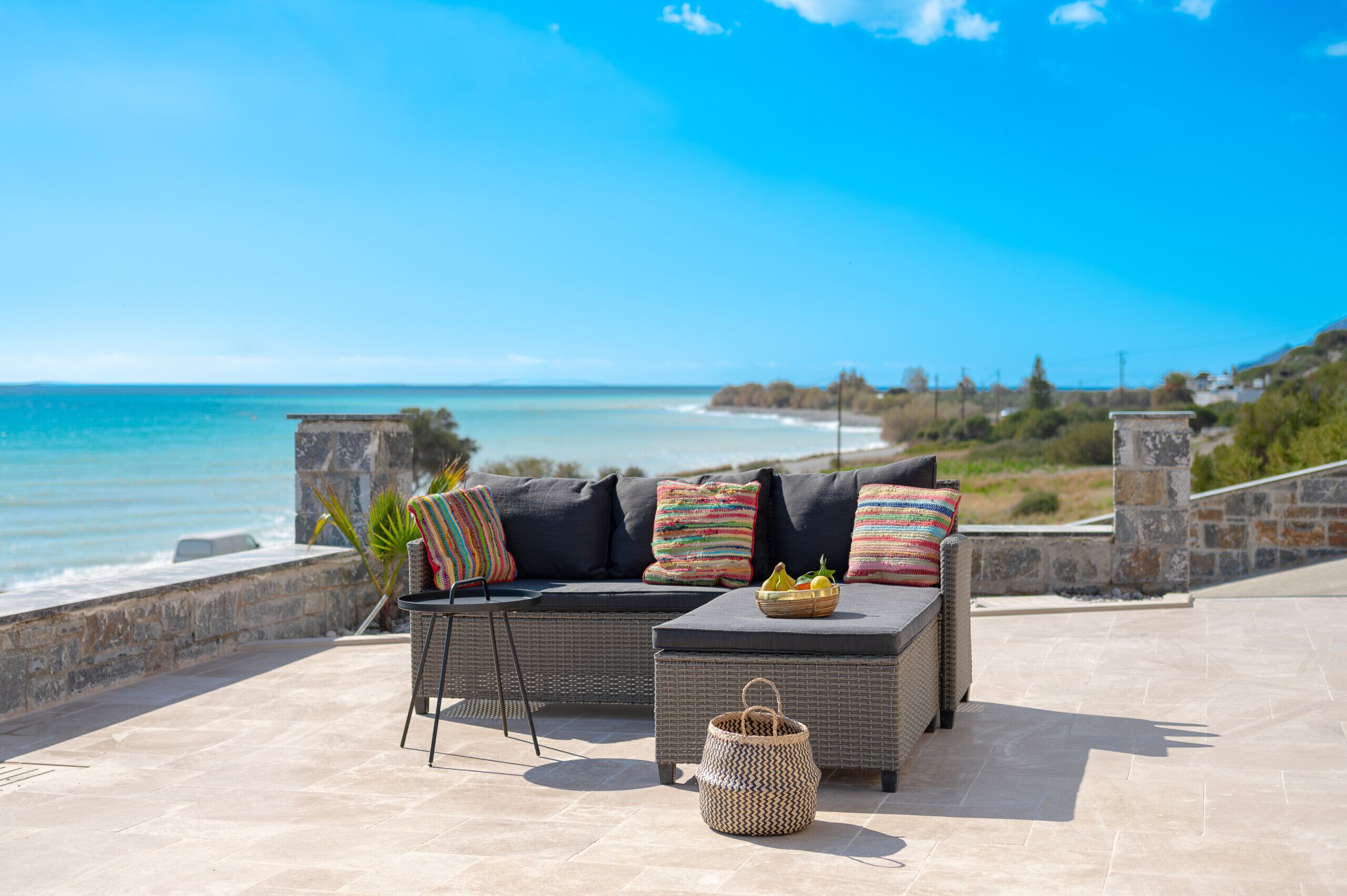 An outdoor seating area with a sofa and a small table, overlooking a beach and ocean.