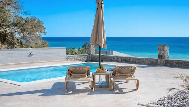 A poolside area with two lounge chairs, a table with a basket of fruit, and a beach view. - Kedros Villa Tessera (Viannos)