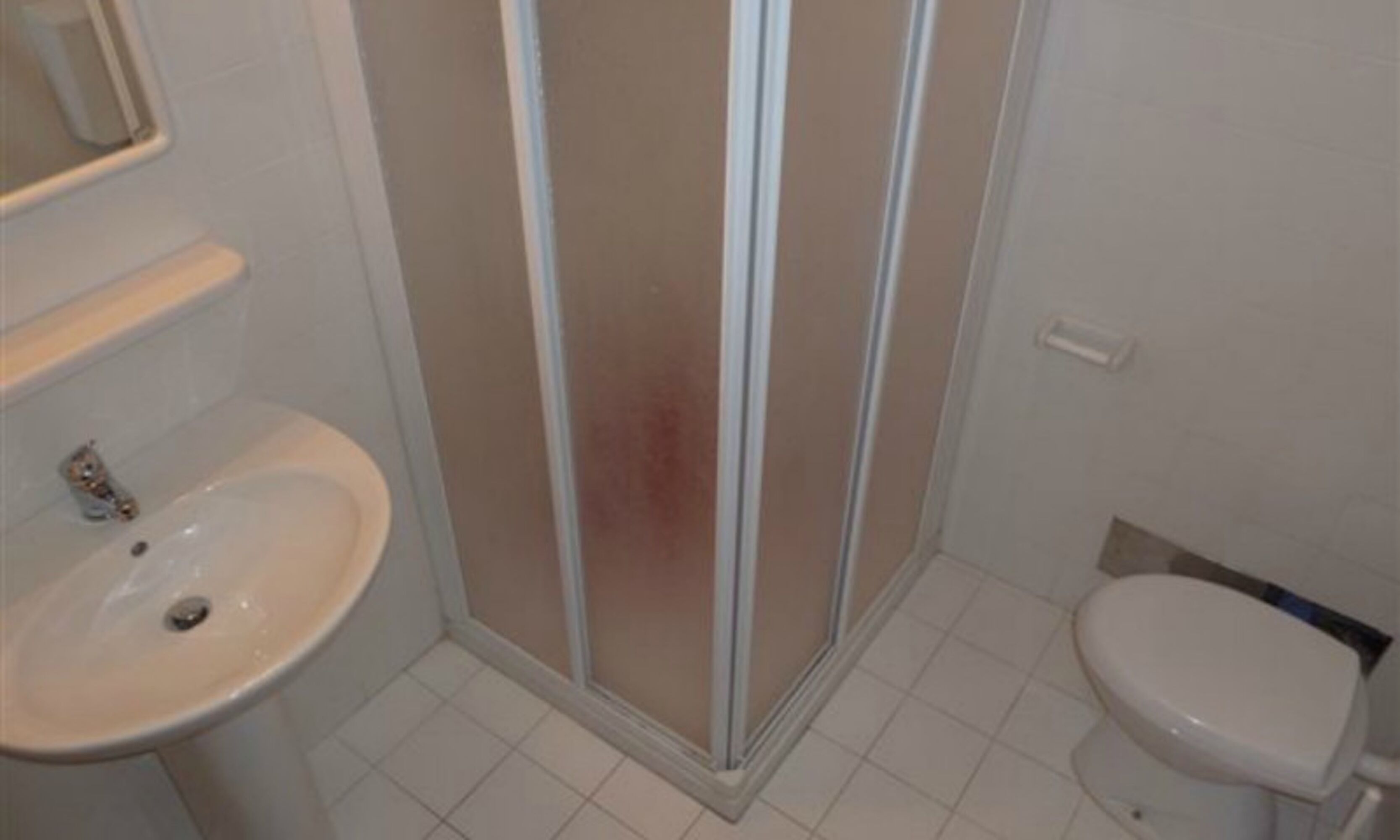 Ein Badezimmer mit weißem Waschbecken, Toilette und einer Duschkabine.