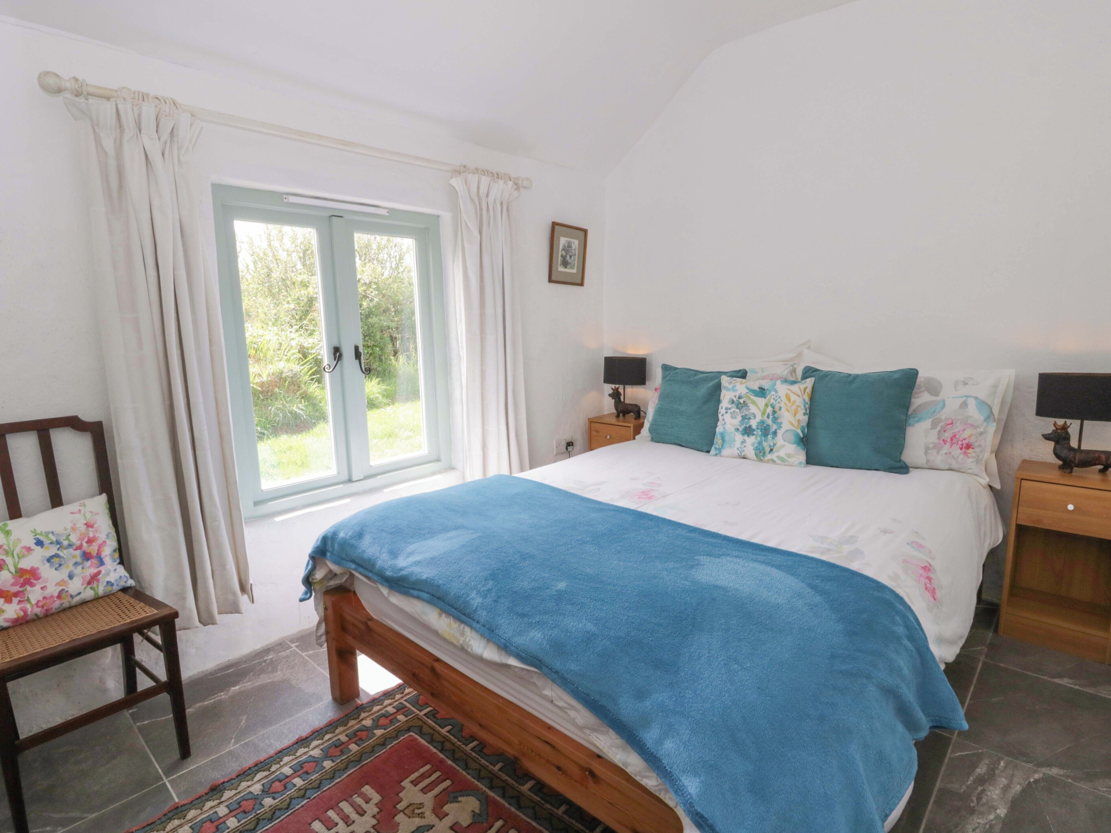 A bedroom with a bed, a nightstand, a chair, a window with curtains, and a rug.