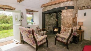 A cozy room with a stone wall, a fireplace, two floral armchairs, and a red bedspread. - Rhos Y Clegyrn (Goodwick)