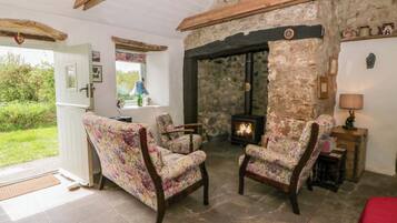 Una habitación acogedora con pared de piedra, chimenea, dos sillones con estampado floral y colcha roja.