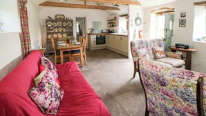 A cozy living room with a red sofa, floral armchairs, wooden beams, a dining table, and a kitchen area. - Rhos Y Clegyrn (Goodwick)