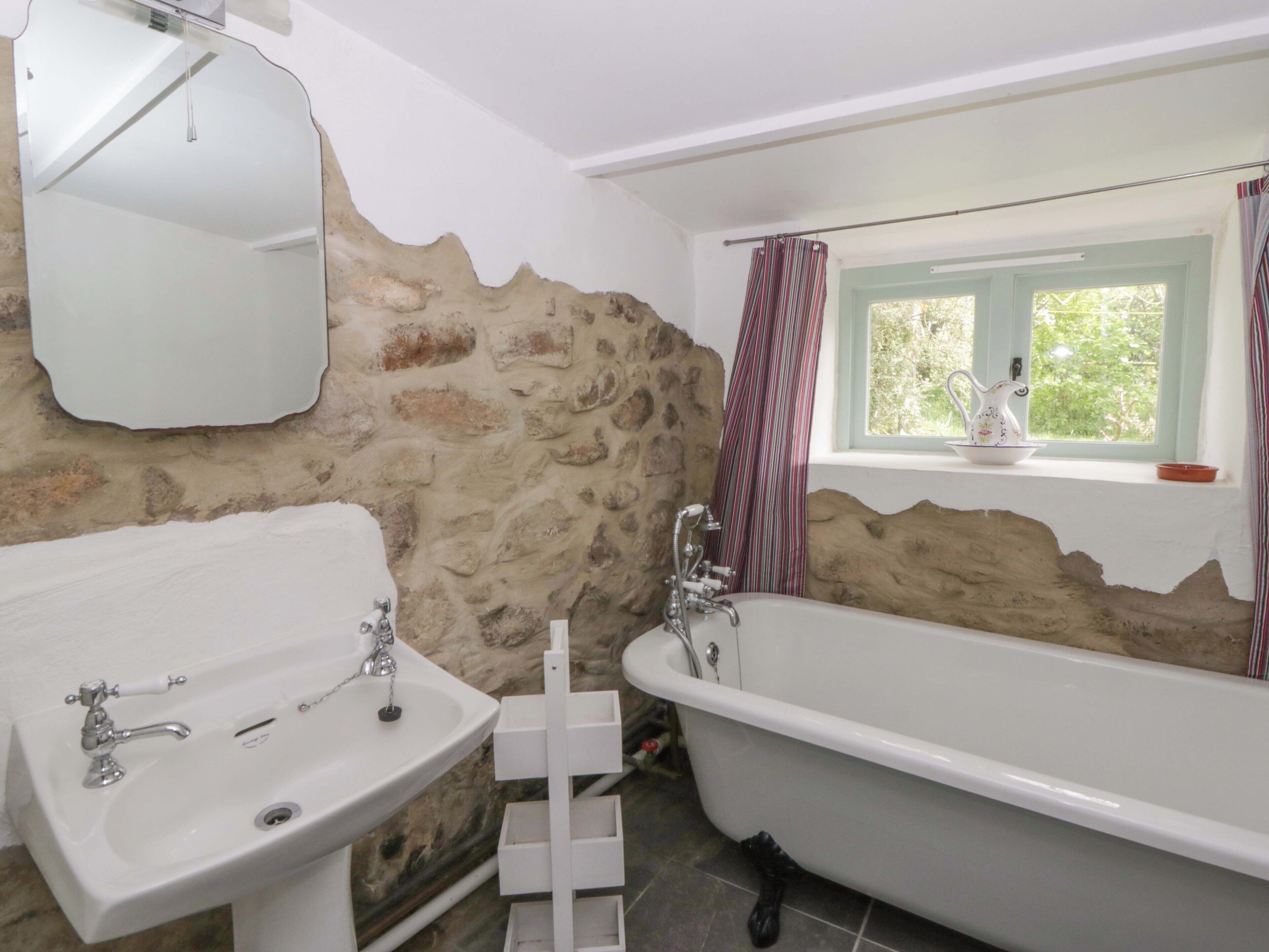 Un baño con pared de piedra, un lavamanos blanco, una bañera y una ventana con vistas.