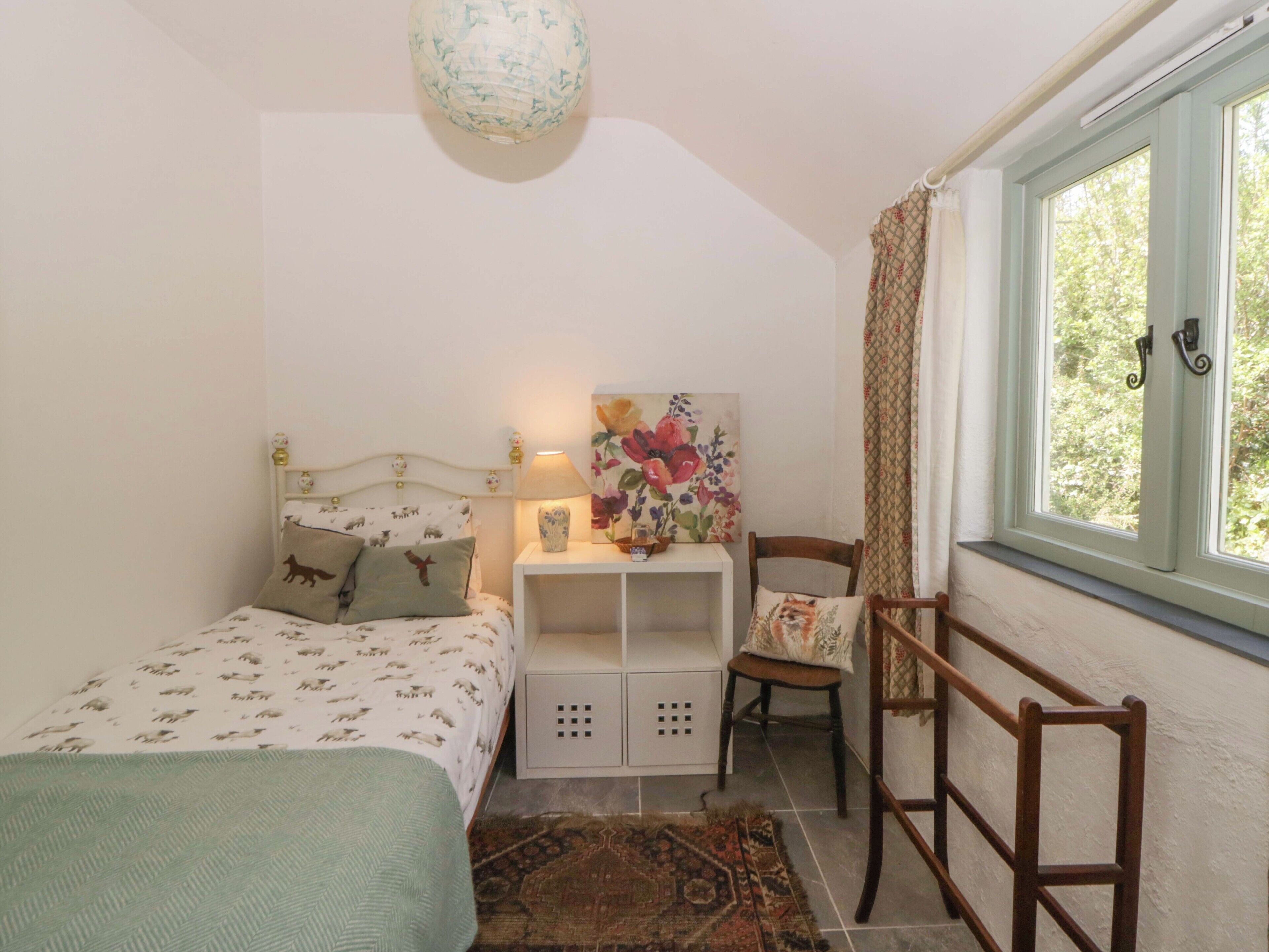 A bedroom with a bed, bedside table, chair, and a window with curtains.