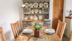 A wooden dining table with white plates, a vase with flowers, and a vintage cabinet in the background. - Rhos Y Clegyrn (Goodwick)