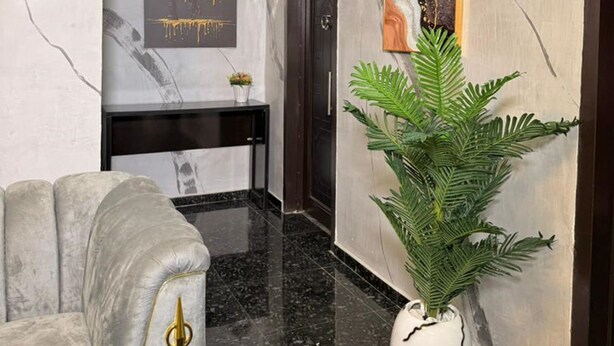 Un hall d’entrée moderne avec un mur en marbre, un comptoir de réception noir, un canapé gris et une grande plante en pot.