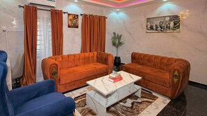 Un salon avec deux canapés orange, un fauteuil bleu, une table basse en marbre et un lustre.