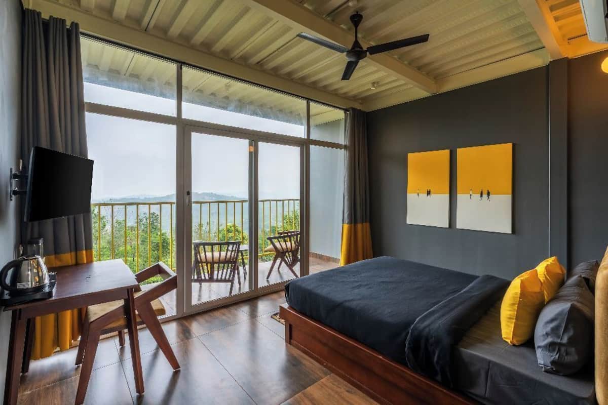 Une chambre avec un lit, un bureau, une chaise et une télévision. Elle possède un balcon avec vue sur le paysage.