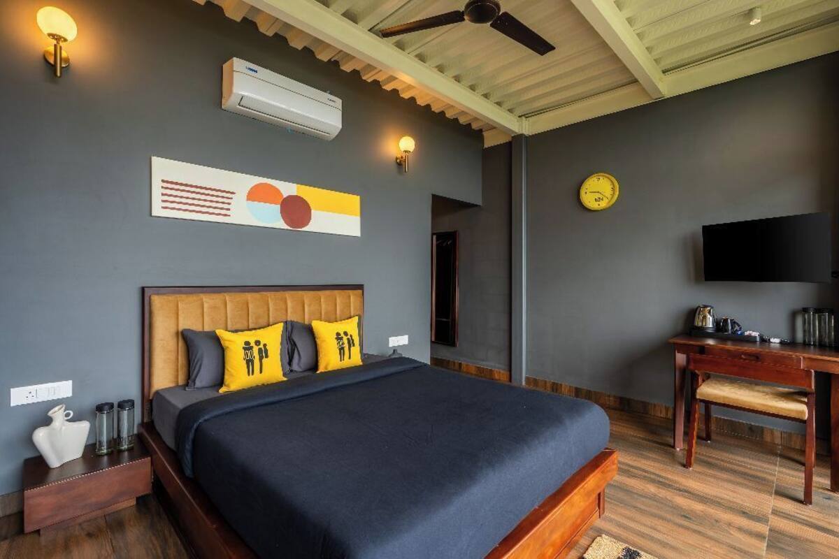 Une chambre d’hôtel moderne dotée d’un grand lit, d’une tête de lit en bois, d’un téléviseur à écran plat, d’un bureau et d’un ventilateur de plafond.