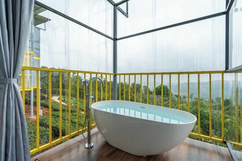 A modern bathroom with a freestanding bathtub, a glass shower enclosure, and a view of a lush landscape through large windows.