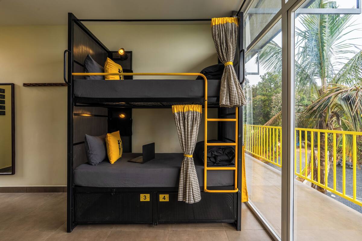 Un lit superposé avec une échelle, un petit bureau et une fenêtre donnant sur des palmiers.