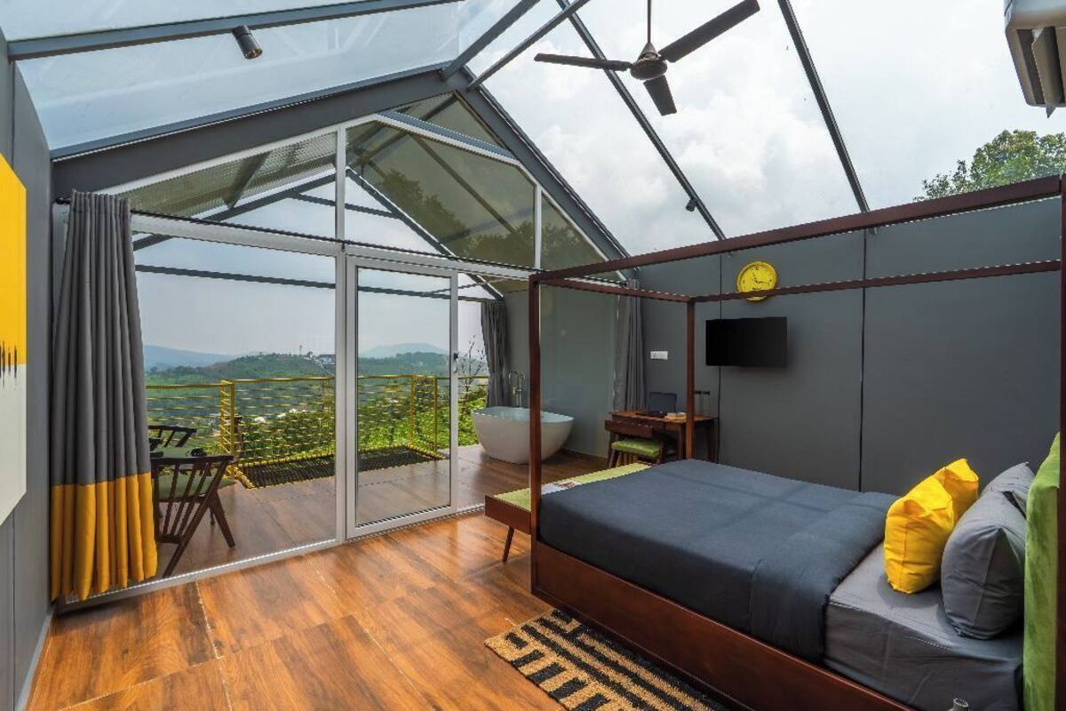 Une chambre moderne avec un grand lit, une vue sur l’extérieur et un mur en verre.