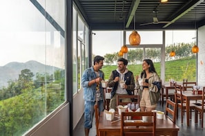 Un restaurante con amplios ventanales que ofrece vistas a un paisaje verde y exuberante y colinas.