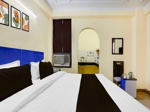 Quarto de hotel com uma cama grande, uma escrivaninha com espelho e uma janela com ar condicionado.
