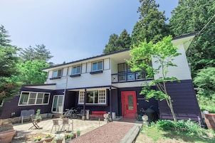 A two-story house with a red door, a balcony, and a garden area with outdoor furniture.