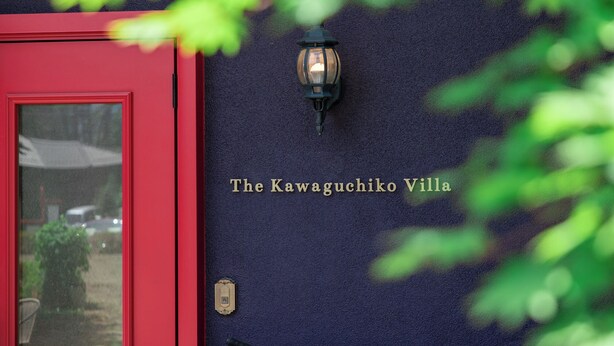 A red door with a wall-mounted light fixture and the text 'The Kawaguchiko Villa' on a dark wall. - Auberge The Kawaguchiko Villa (Fujikawaguchiko)