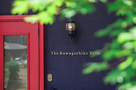 A red door with a wall-mounted light fixture and the text 'The Kawaguchiko Villa' on a dark wall.