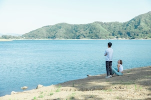 Una pareja junto a un lago, con una colina boscosa al fondo.