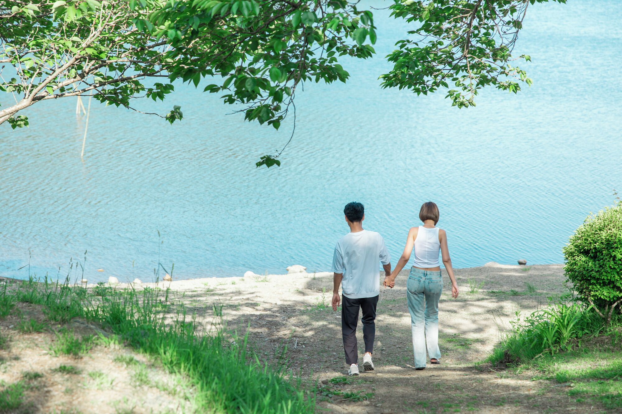 Two people walking on a dirt path with a body of water in the background.