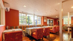 A restaurant with wooden floors, tables with white tablecloths, and red patterned chairs. - Auberge The Kawaguchiko Villa (Fujikawaguchiko)
