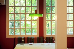 Una mesa de comedor con copas de vino, una lámpara colgante verde y una ventana con vistas a la vegetación.