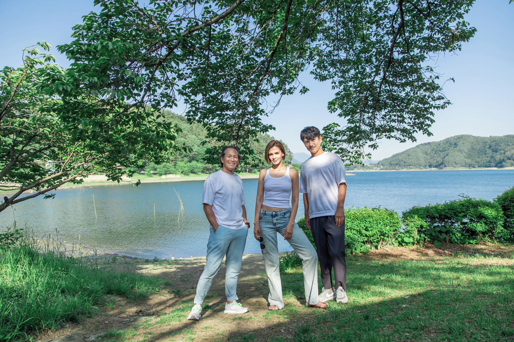 Three people standing outdoors with a lake and hills in the background.