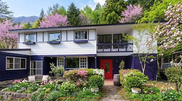 A two-story house with a red door, a balcony, and a garden with various plants and flowers.