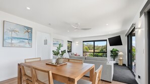 Un moderno salón con una mesa de comedor de madera, un sofá gris y un televisor montado en la pared.