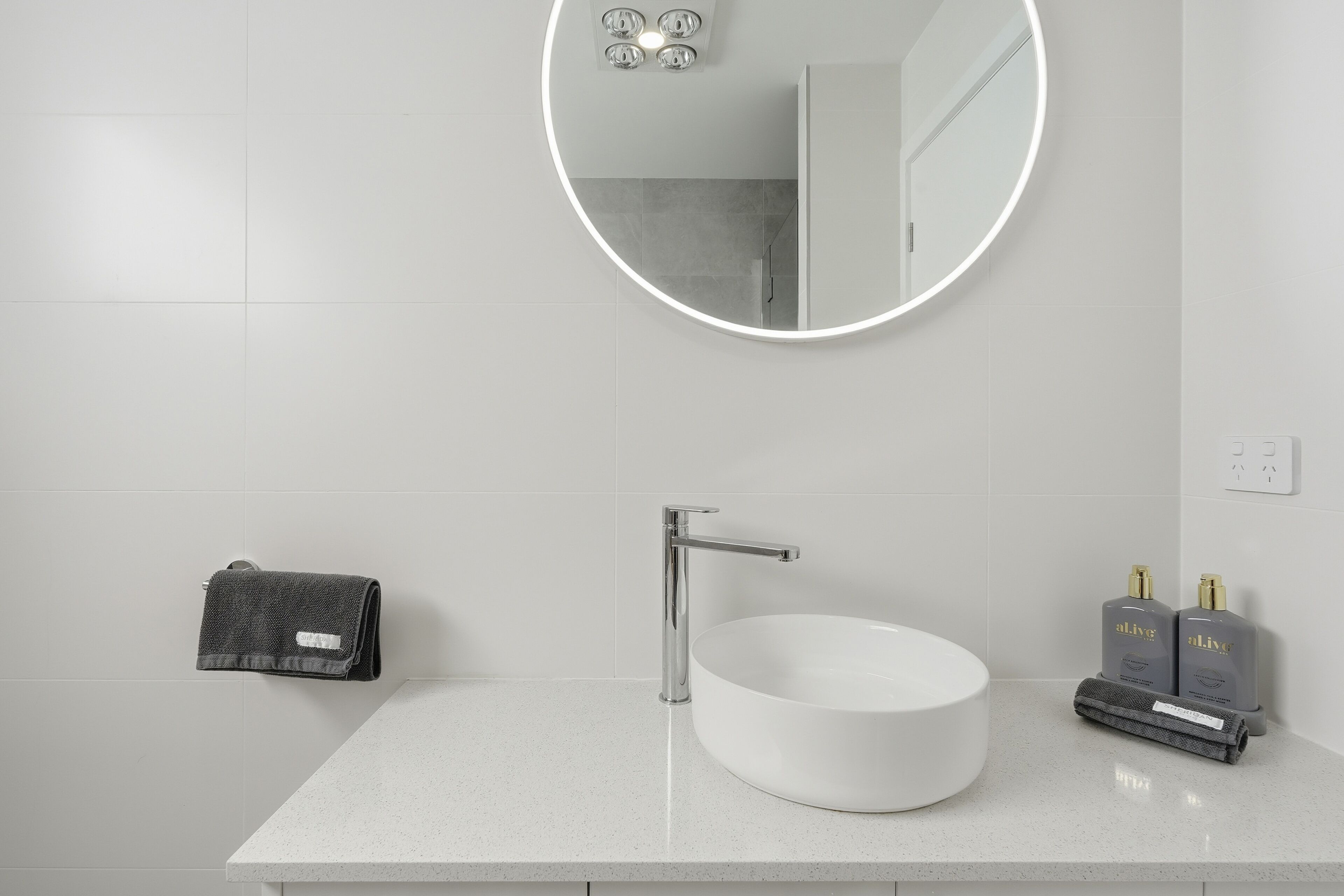 A bathroom with a round mirror, a white sink, and two bottles of toiletries.