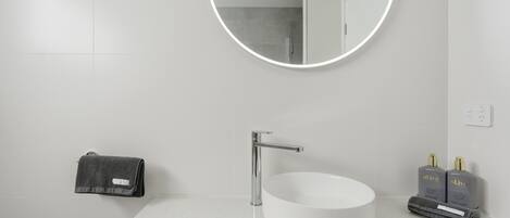 A bathroom with a round mirror, a white sink, and two bottles of toiletries.