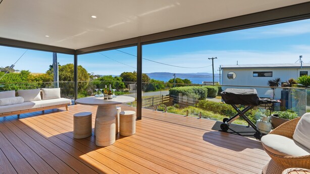 Una terraza moderna al aire libre con sofá, mesa redonda y zona de barbacoa, con vistas a un paisaje pintoresco.
