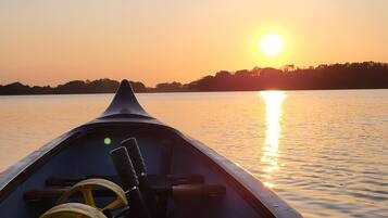Bootinterieur met een stuurwiel en uitzicht op een ondergaande zon over het water.