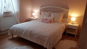 Ein Schlafzimmer mit einem Bett, zwei Nachttischen mit Lampen, einem Heizkörper und einem Fenster mit Vorhängen.
