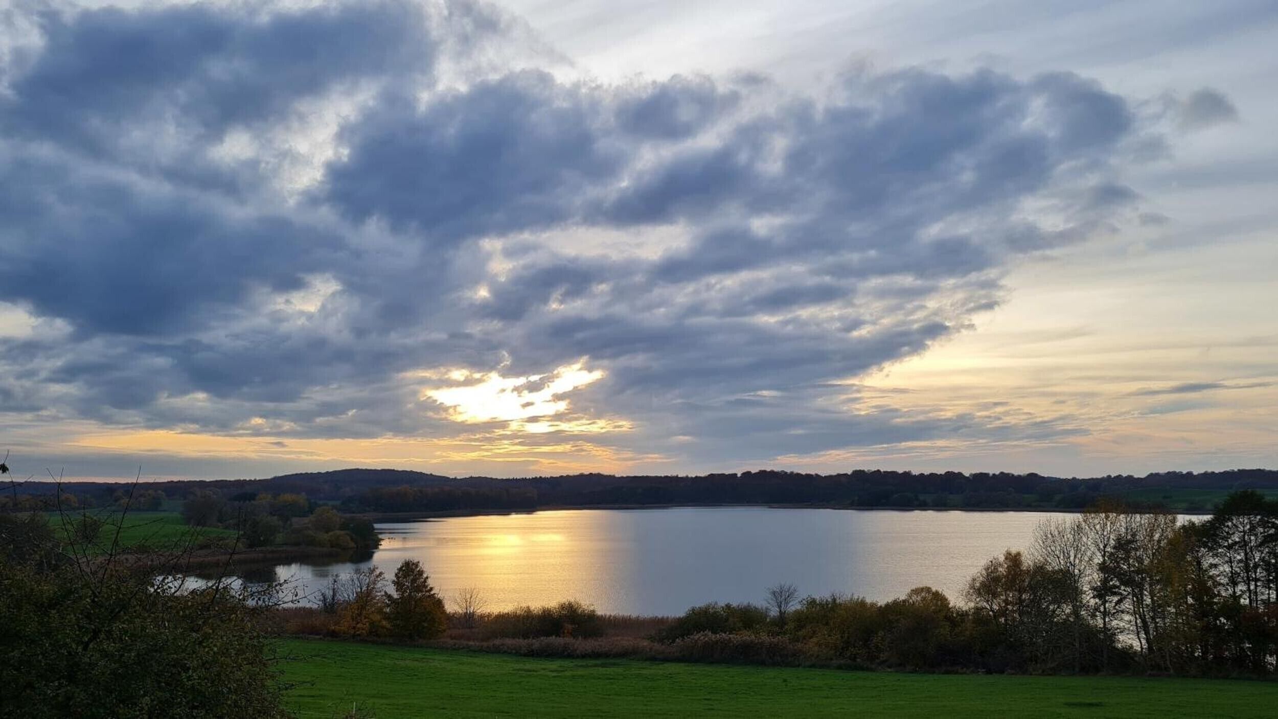 Ein See mit bewölktem Himmel und Sonnenuntergang.
